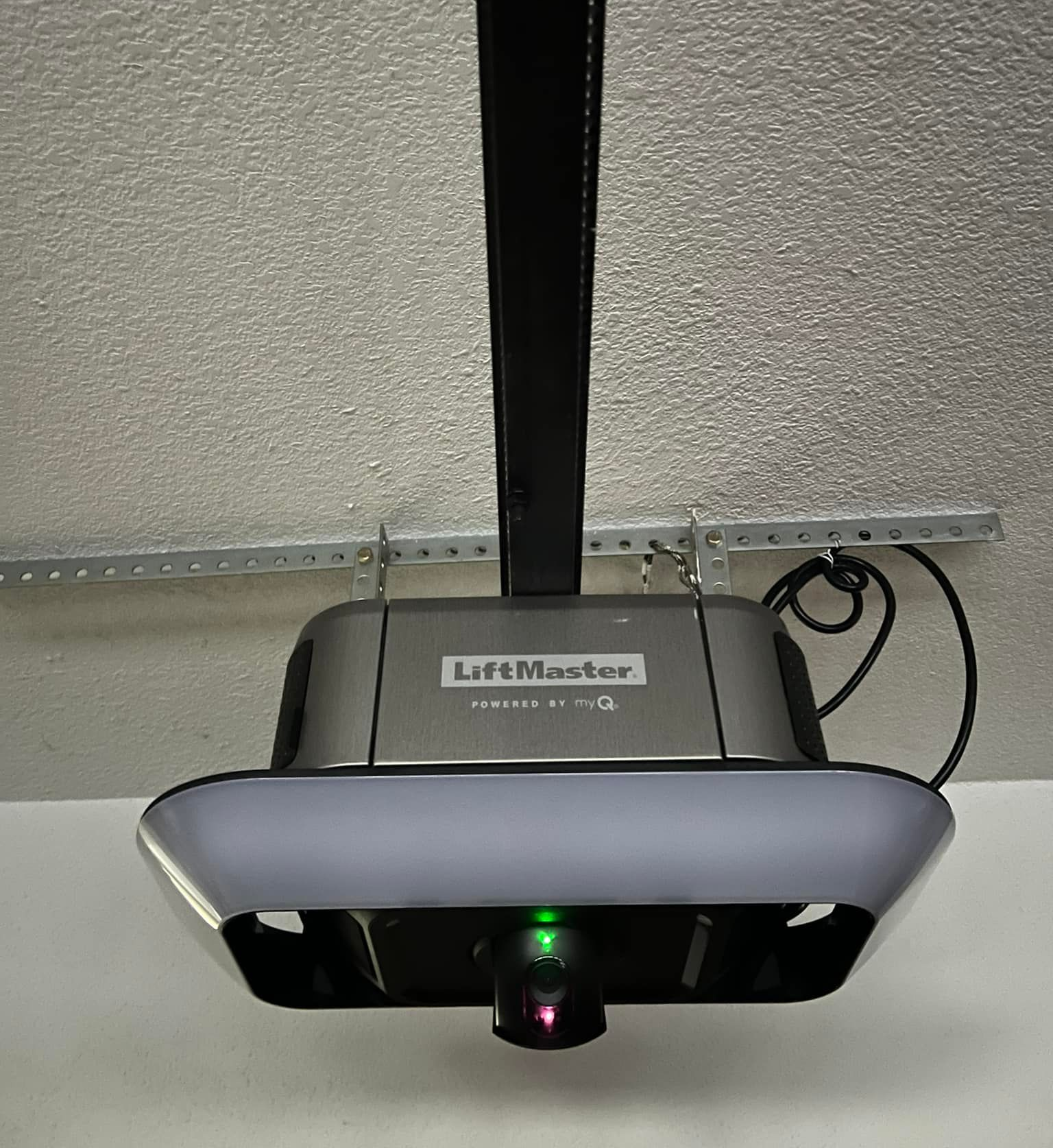 LiftMaster garage door opener with a green light illuminated. Black and gray, mounted to the ceiling.