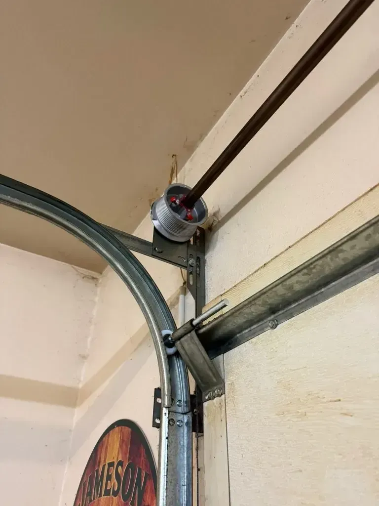 Garage door spring assembly with a metal track, mounted on a white wall.