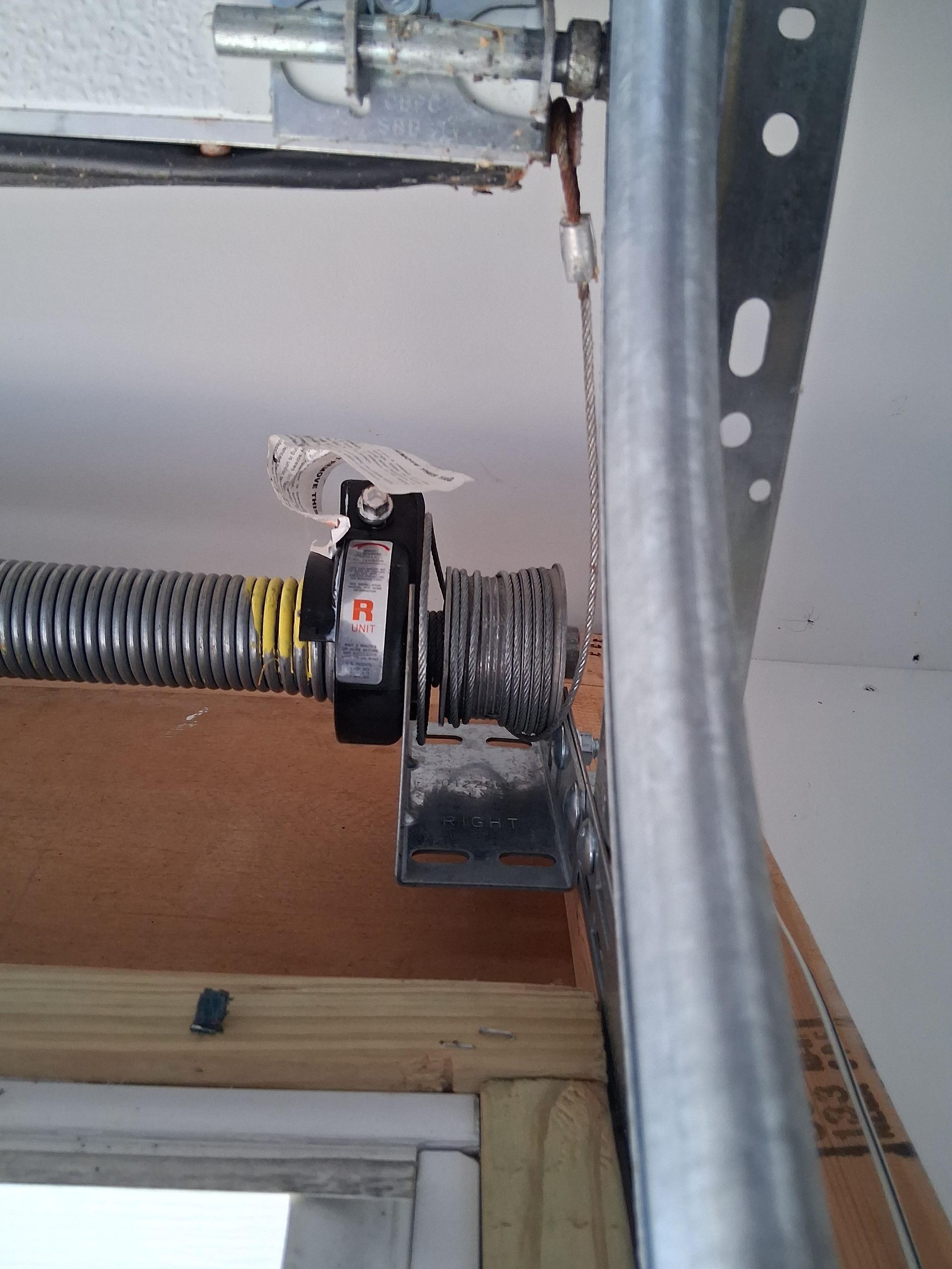 Garage door torsion spring assembly, with a broken spring, near the garage door frame.