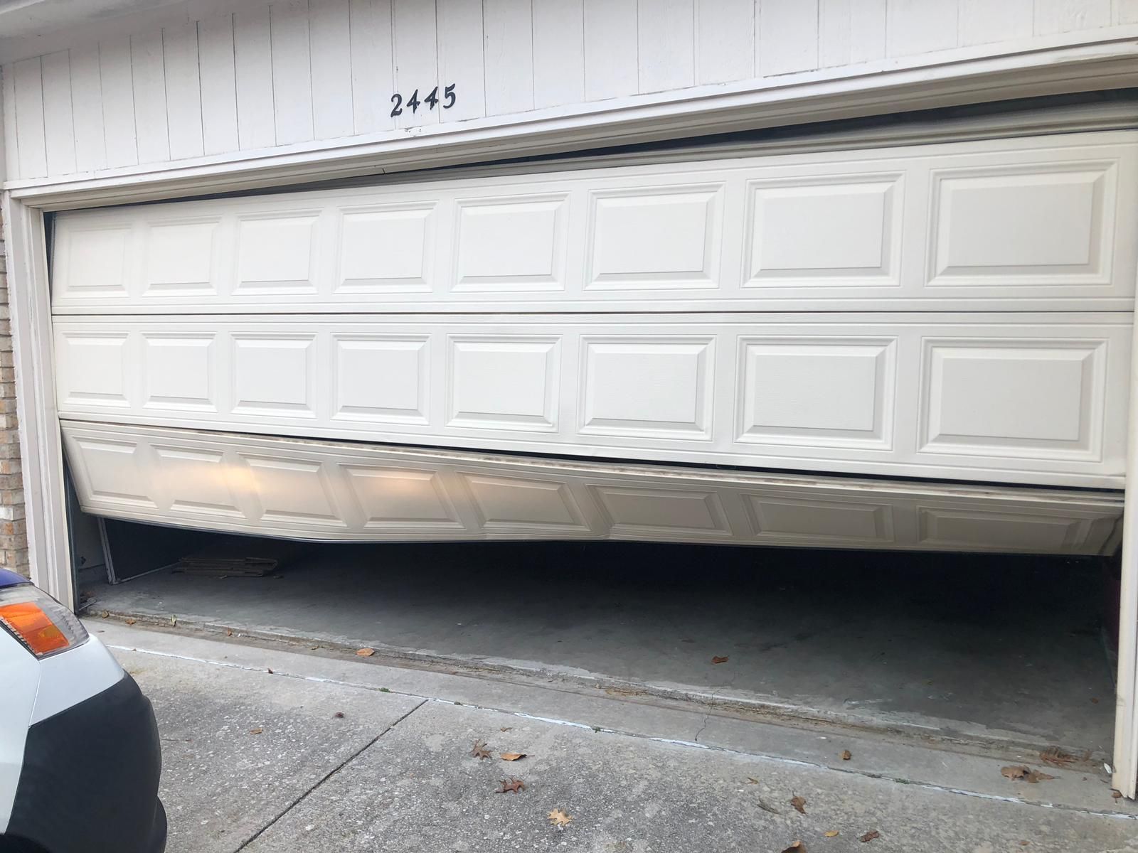 Garage door, partially open and bent, causing obstruction. House number