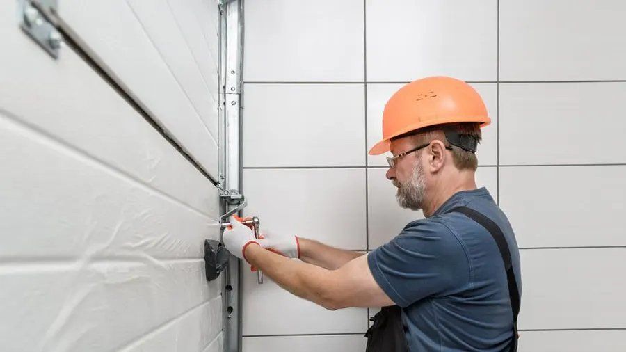 A worker in a hard hat and gloves repairs a white garage door.
