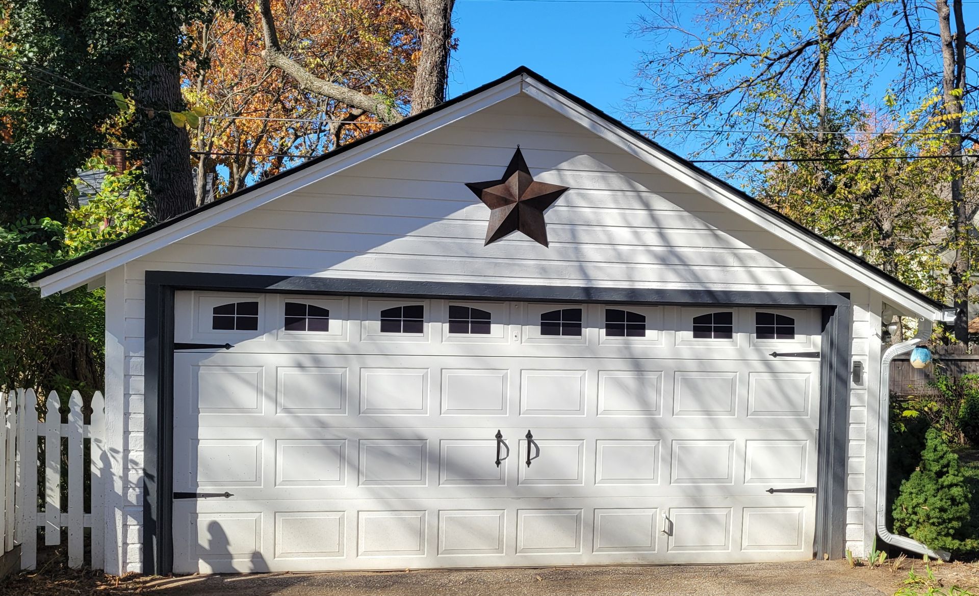 White garage with black trim, star decor, and a white picket fence.