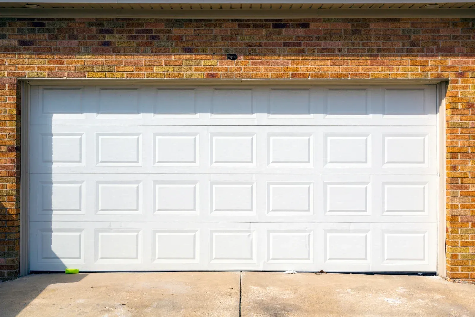 White panel garage door on a brick building with a concrete driveway.