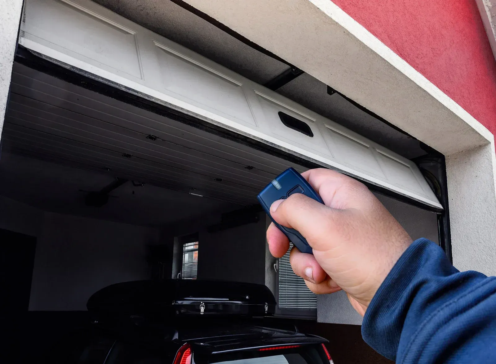 Hand using remote to open garage door; car inside.