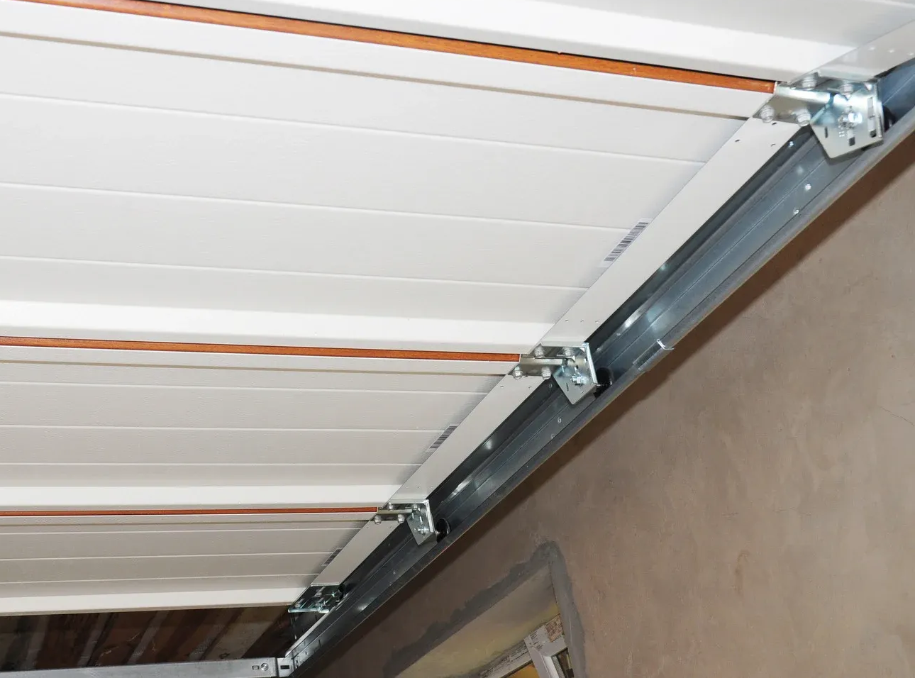 White garage door panels with metal support framing and hinges. Copper wire runs along the ceiling.
