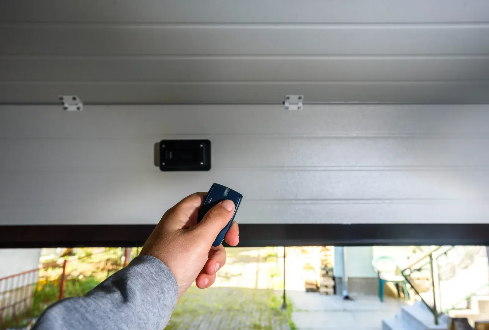 Hand holding a remote control operating a garage door opener.