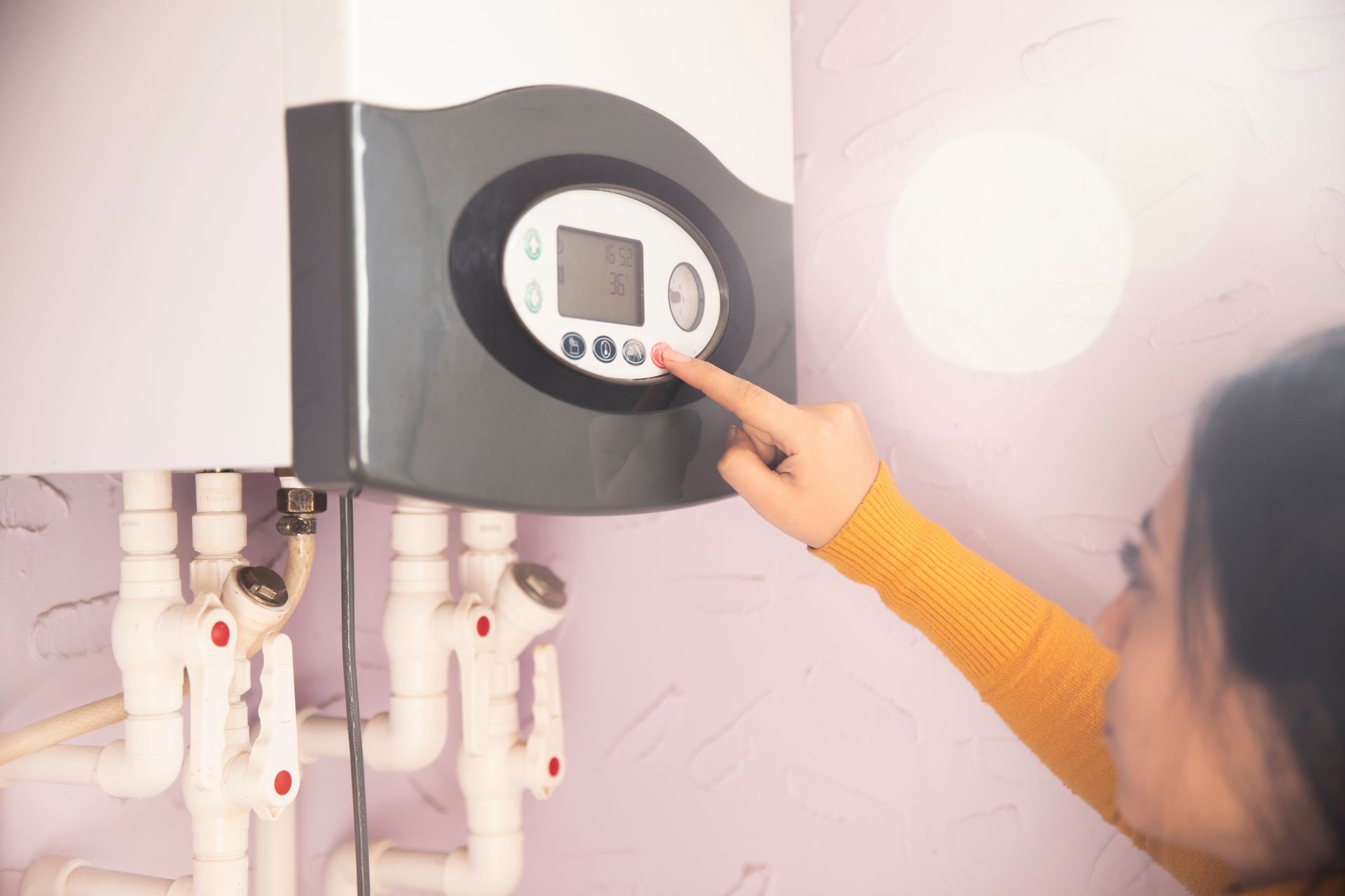 Person using a wall-mounted water heater control panel in a bathroom or utility room