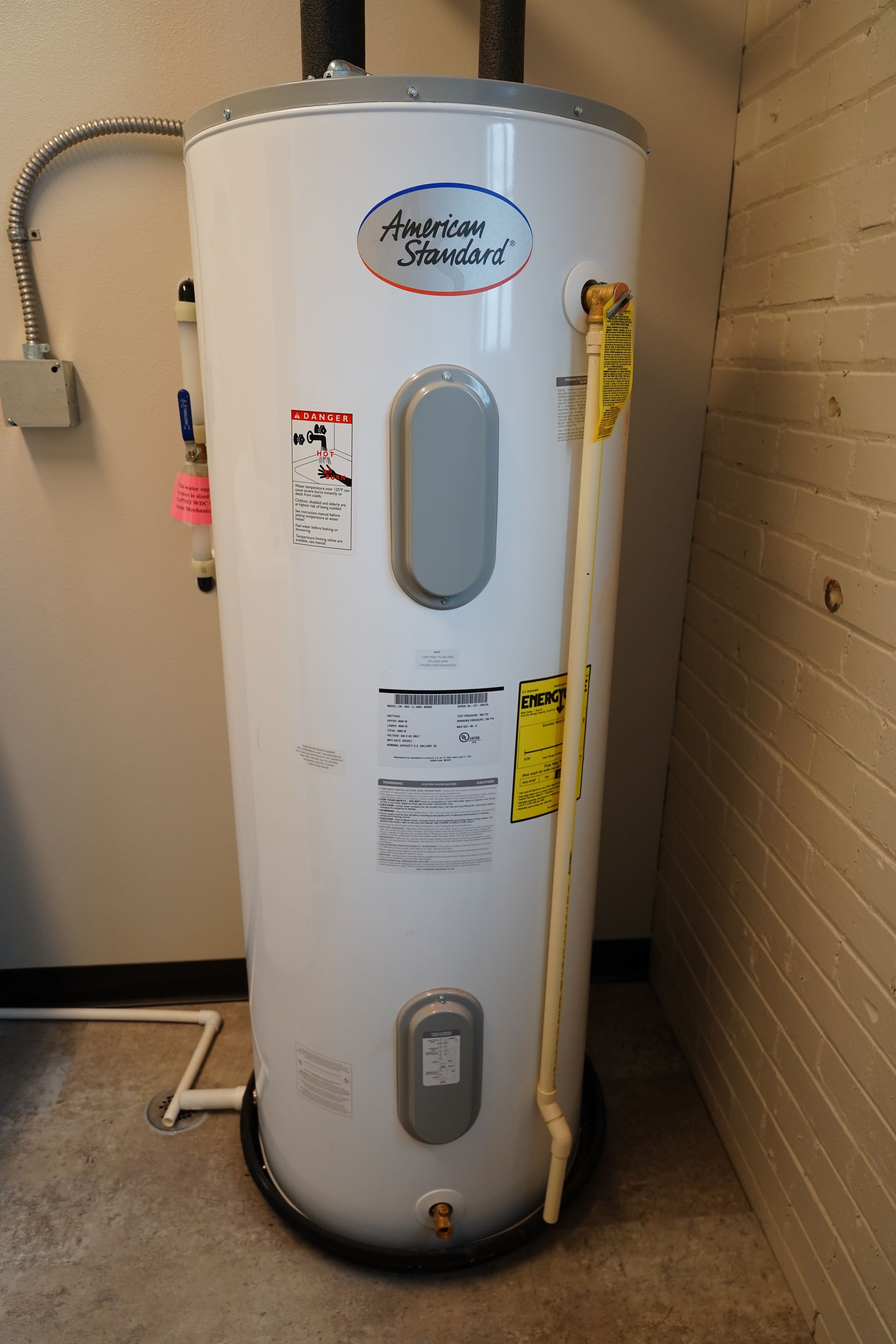 White water heater tank in a utility room against a brick wall, with labels and a small window panel.