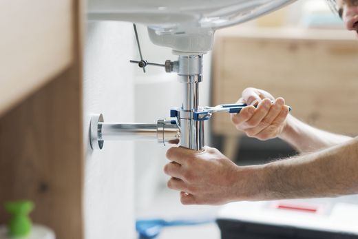 Hands tightening a wrench under a sink drain pipe during plumbing repair