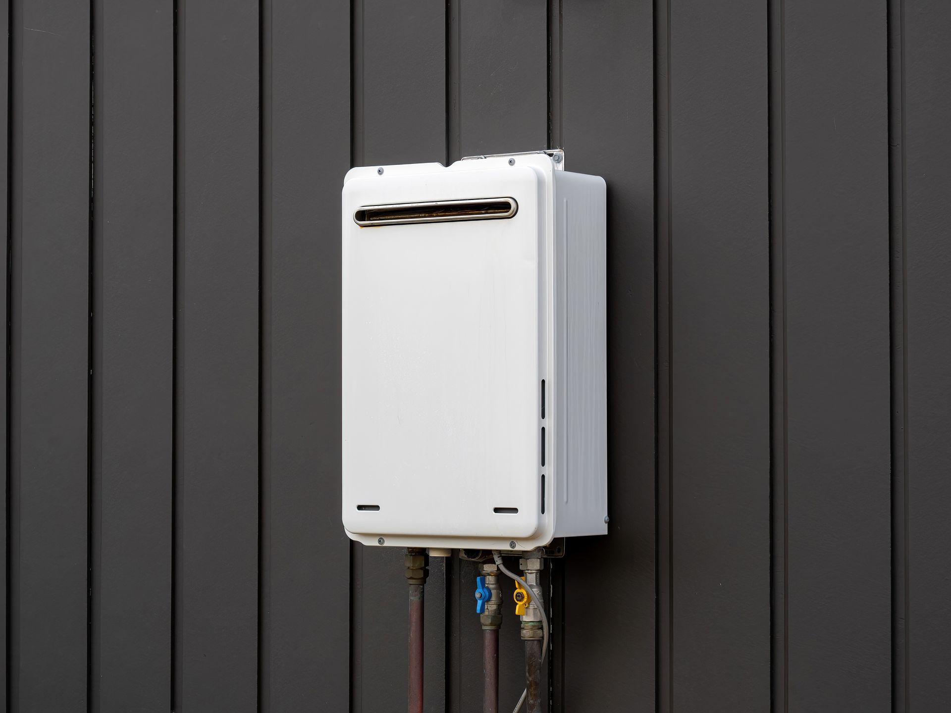 White wall-mounted appliance with pipes and wires against a dark gray paneled wall