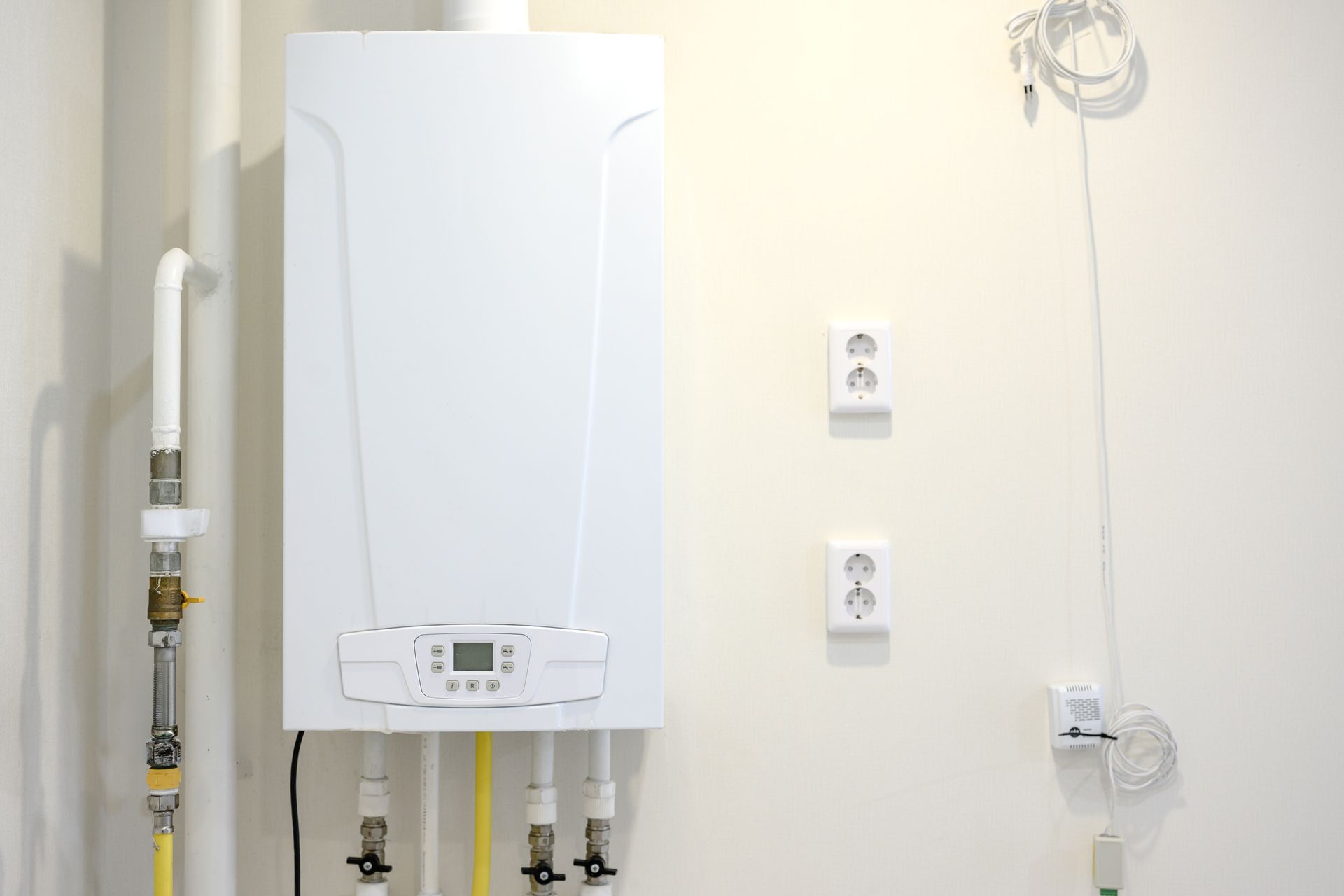 White wall-mounted boiler with exposed pipes and outlets in a utility room