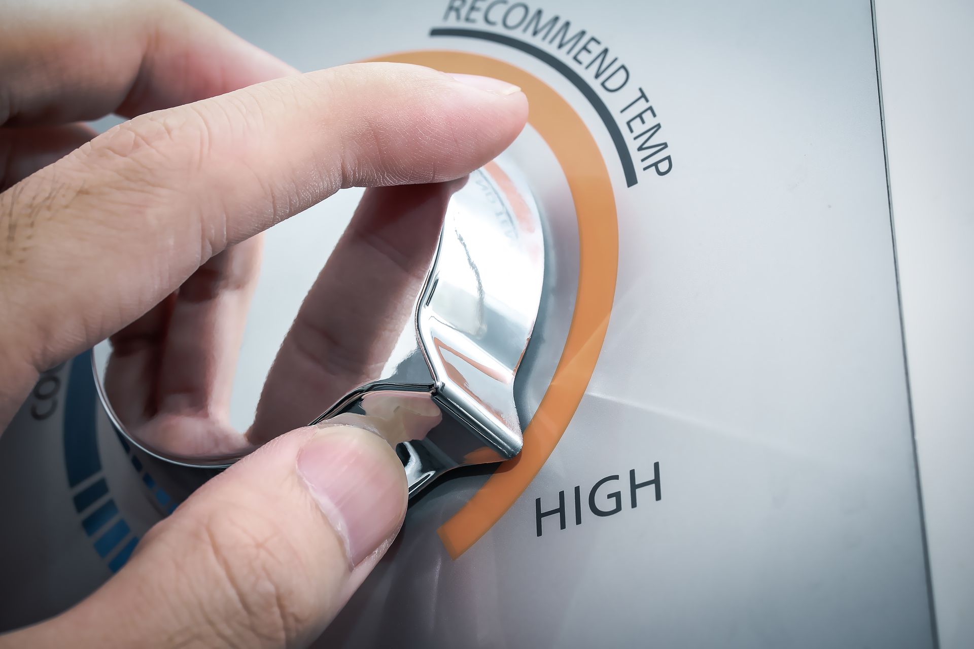 Hand turning a temperature dial toward HIGH and RECOMMENDED TEMP on an appliance panel