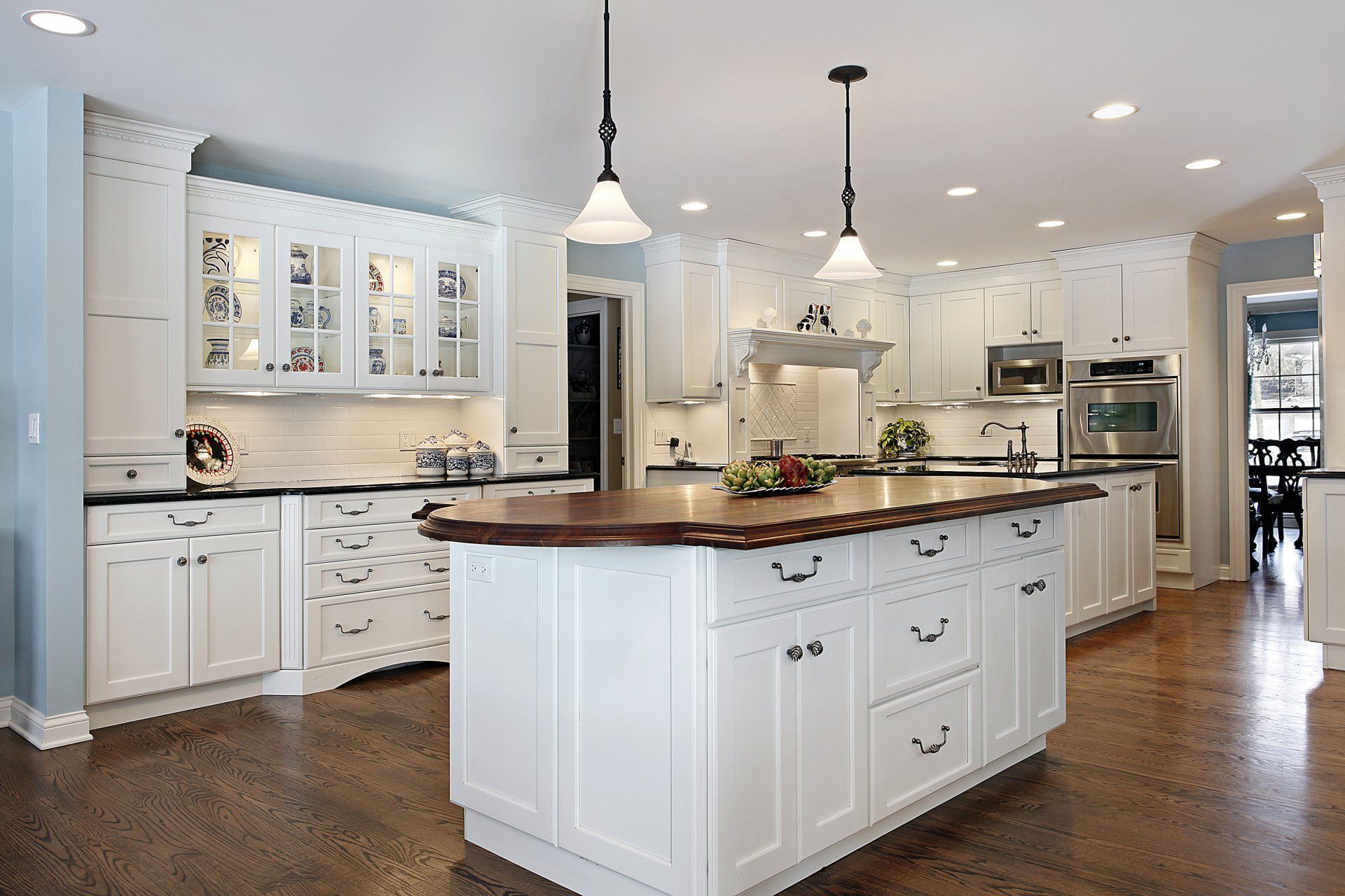 White kitchen with island and wood countertops, pendant lights, and dark wood floors.