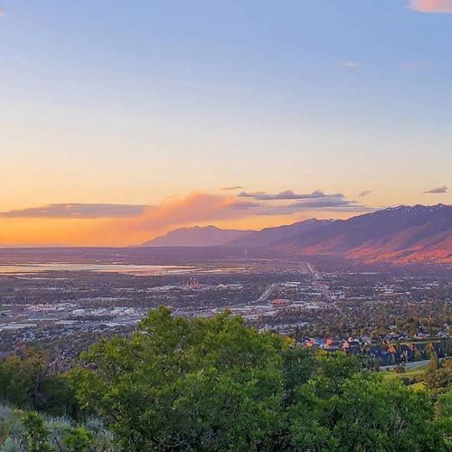 Cityscape at sunset with mountains, a lake, and trees in the foreground. Cityscape at sunset with mountains, a lake, and trees in the foreground.
