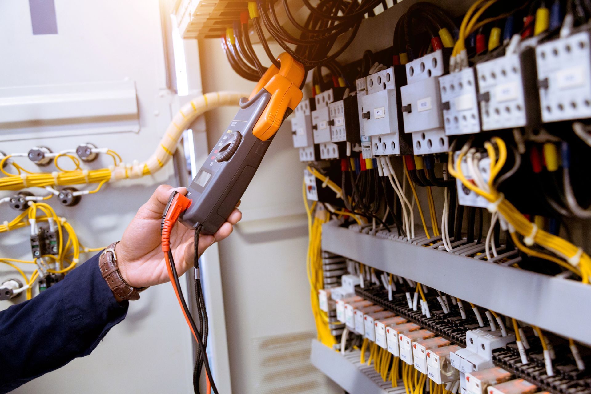 Un tecnico utilizza un amperometro a pinza per misurare la corrente nei cavi elettrici all'interno di un quadro elettrico.