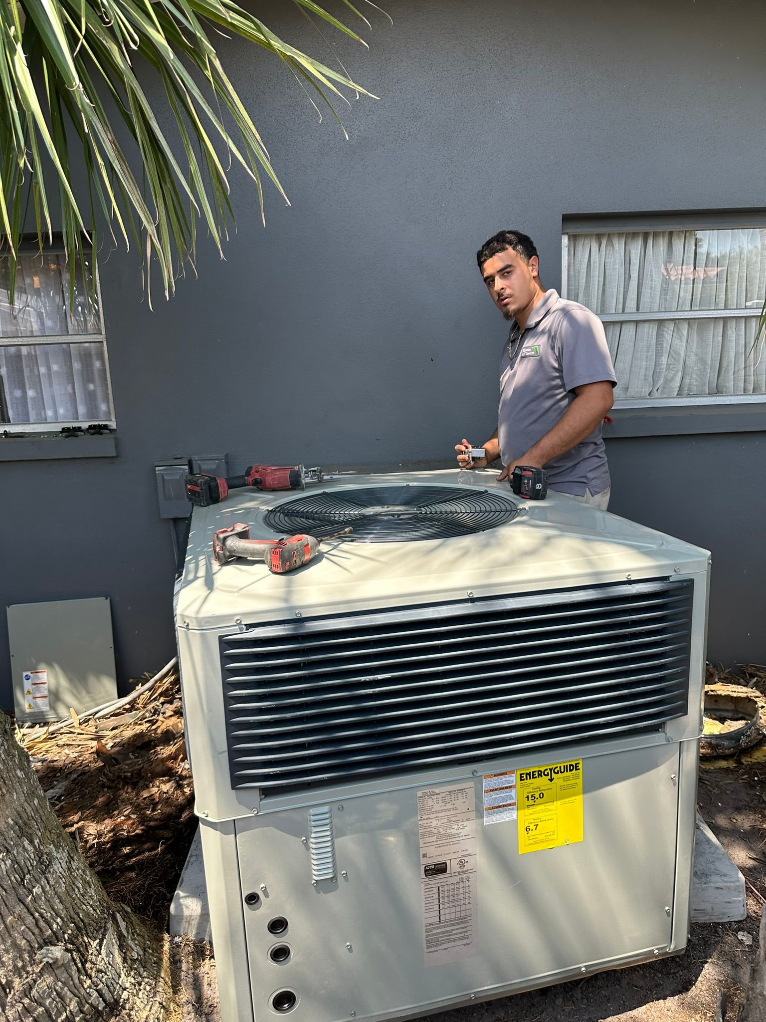 Technician standing beside rooftop HVAC unit outdoors by a building wall