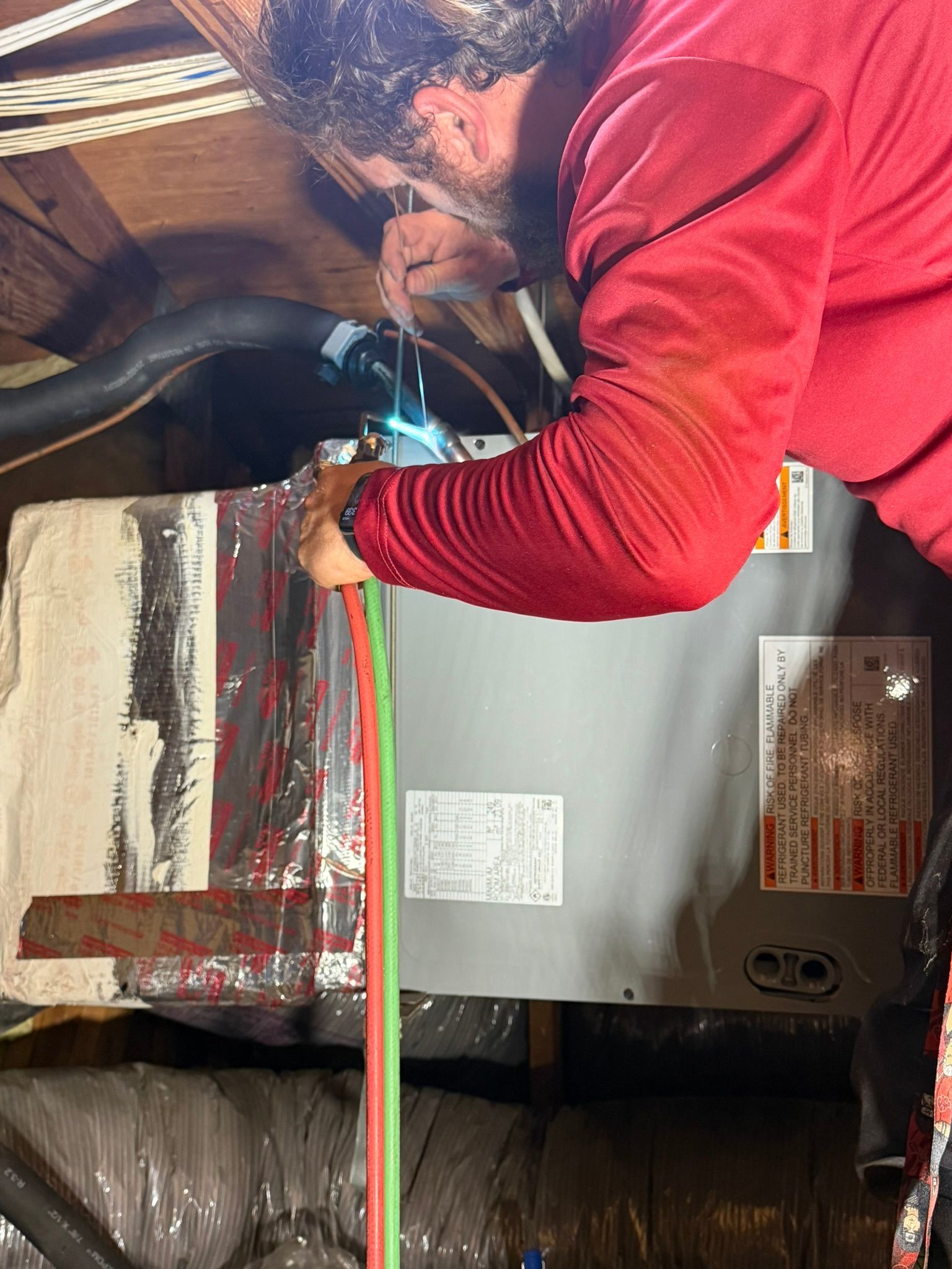 Person in red jacket using a tool on a metal surface in an industrial setting