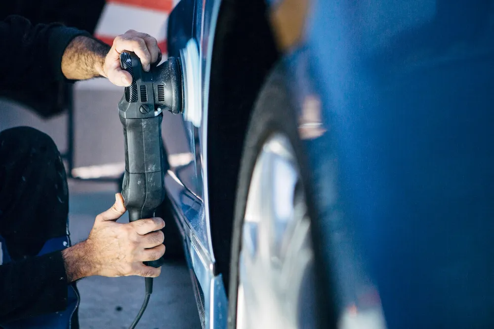 Person using a power buffer on a blue car door.