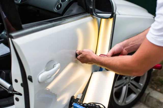 Person using tools to remove a dent from a white car door.