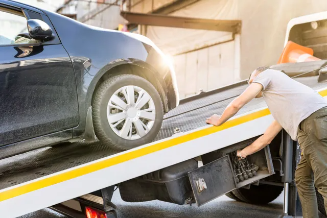 Black car being loaded onto a tow truck by a person in a light gray shirt.