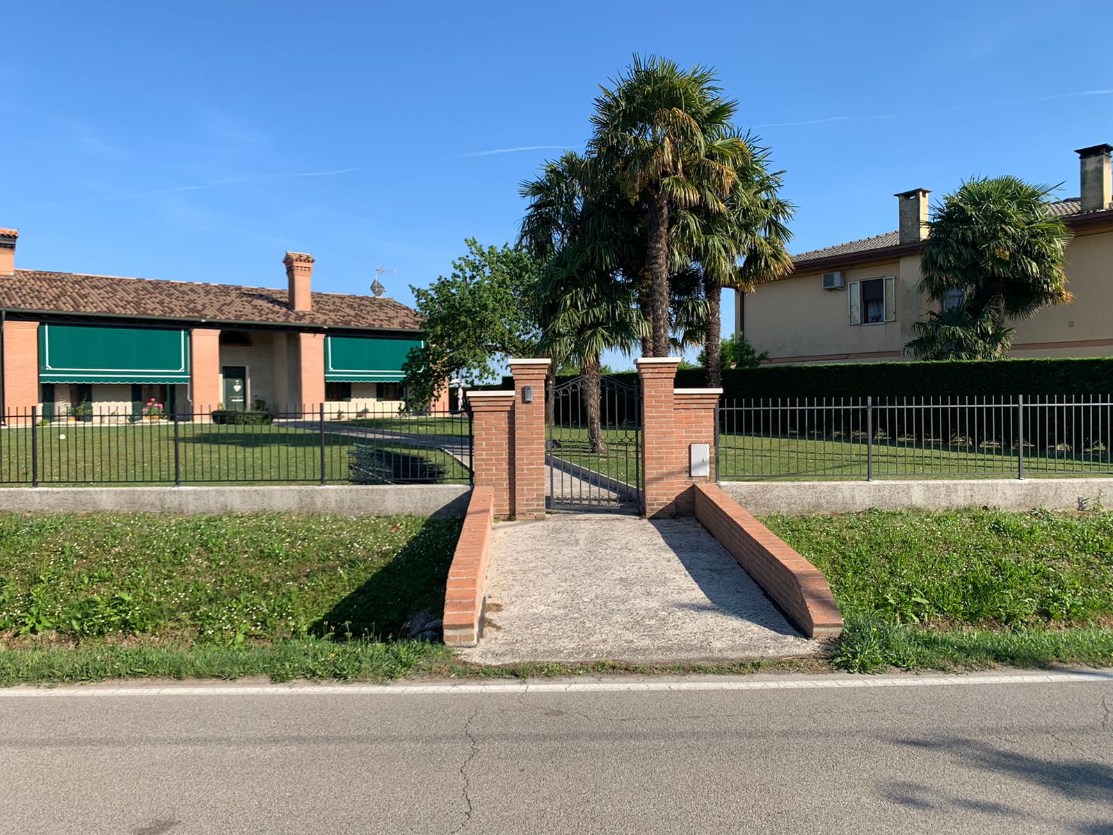 Porta in mattoni e sentiero che conduce alle case, con una palma, in una giornata di sole.