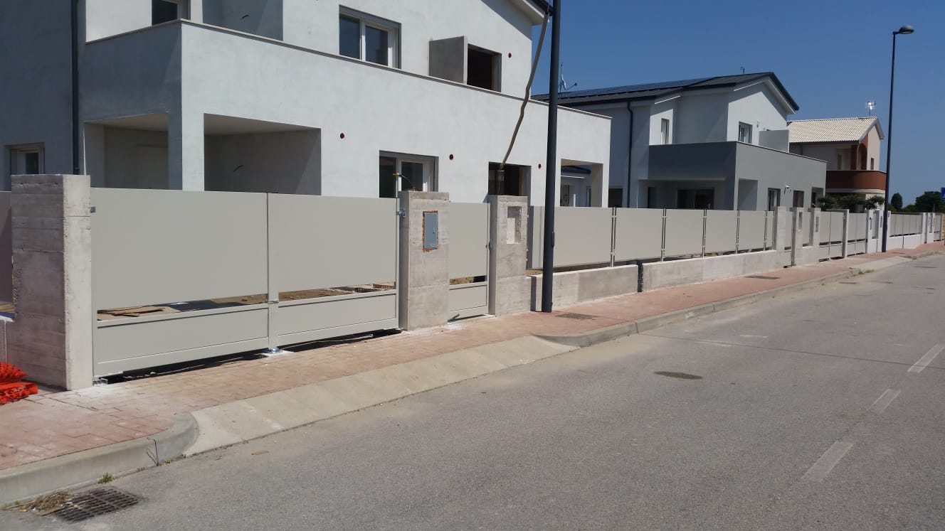 Recinzione in cemento grigio lungo una strada di fronte a case a due piani.
