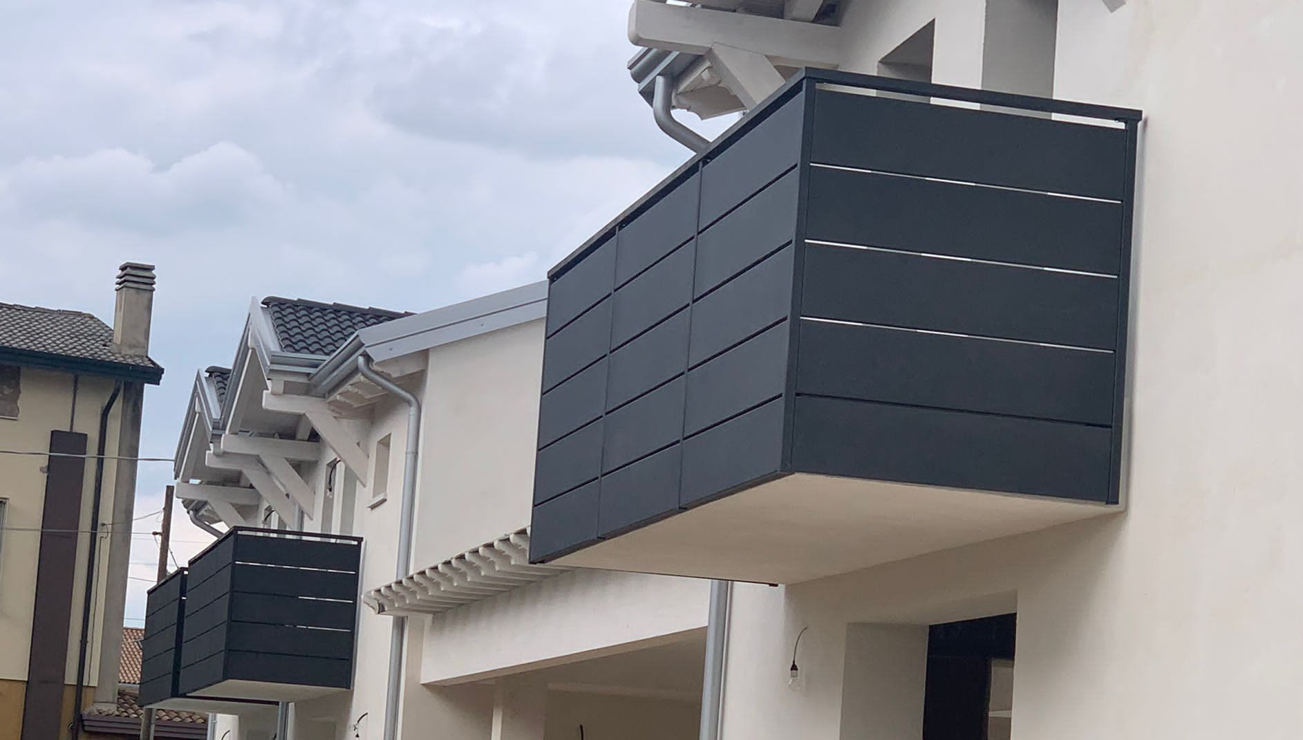 Balconi grigio scuro su un edificio bianco, sullo sfondo di un cielo nuvoloso.