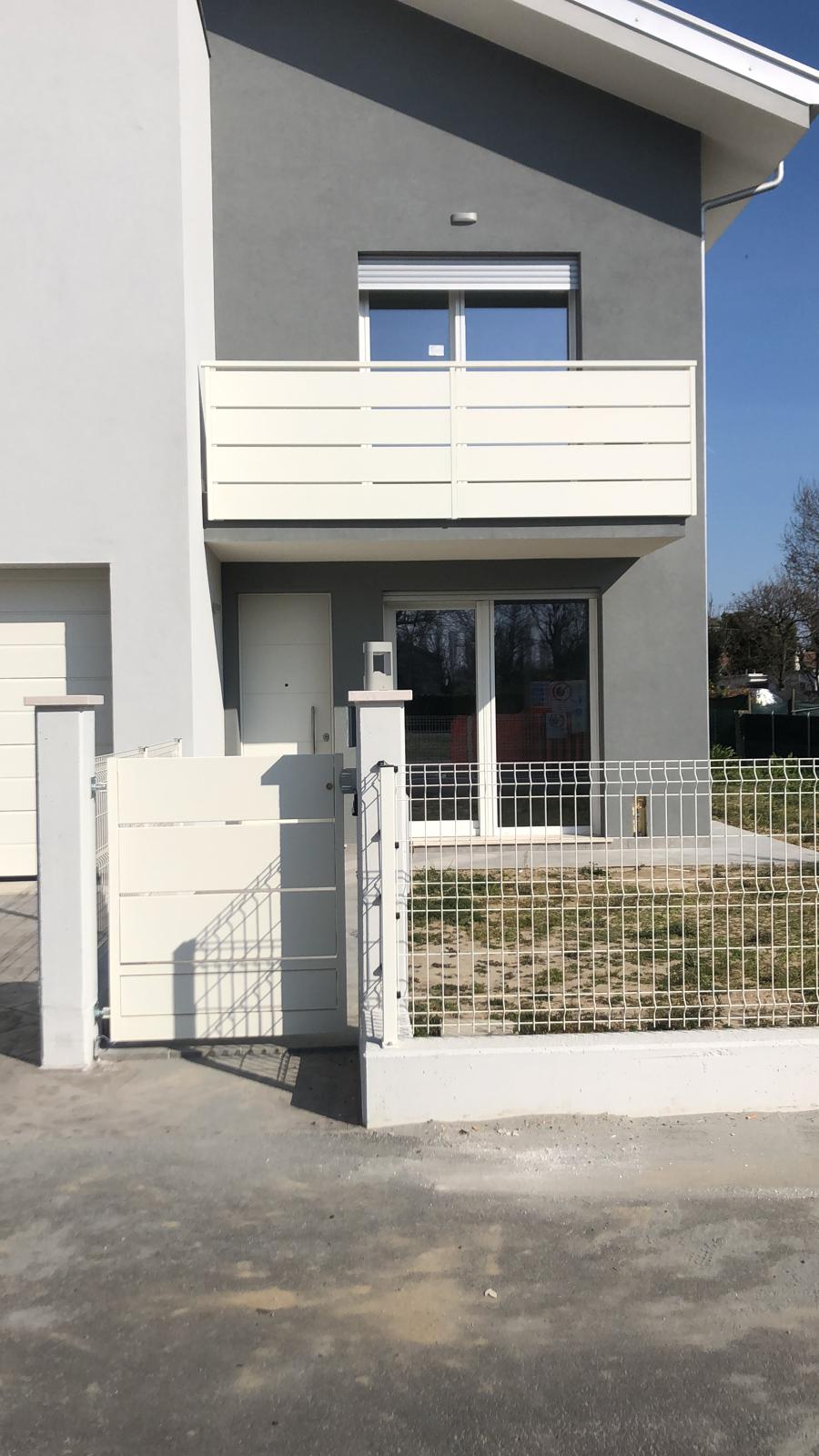 Moderna casa a due piani con facciata grigia e bianca, balcone, porta d'ingresso e cancello d'ingresso.