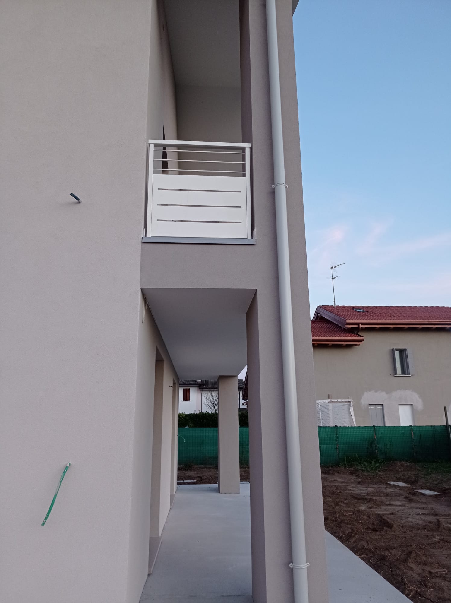 Vista esterna di un edificio con un balcone bianco e una passerella in cemento.