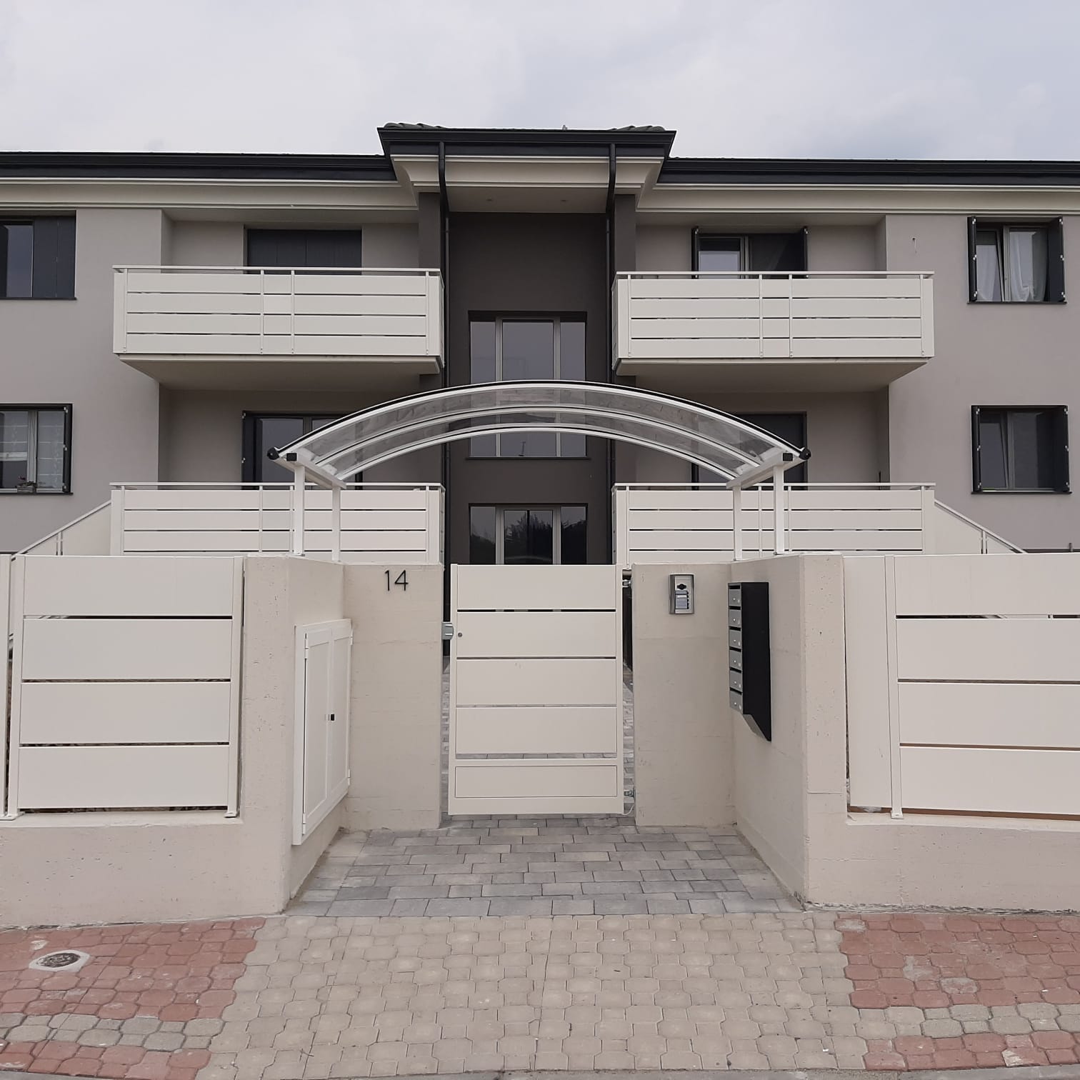 Edificio residenziale con balconi e recinzione bianchi, facciata grigia, ingresso ad arco.