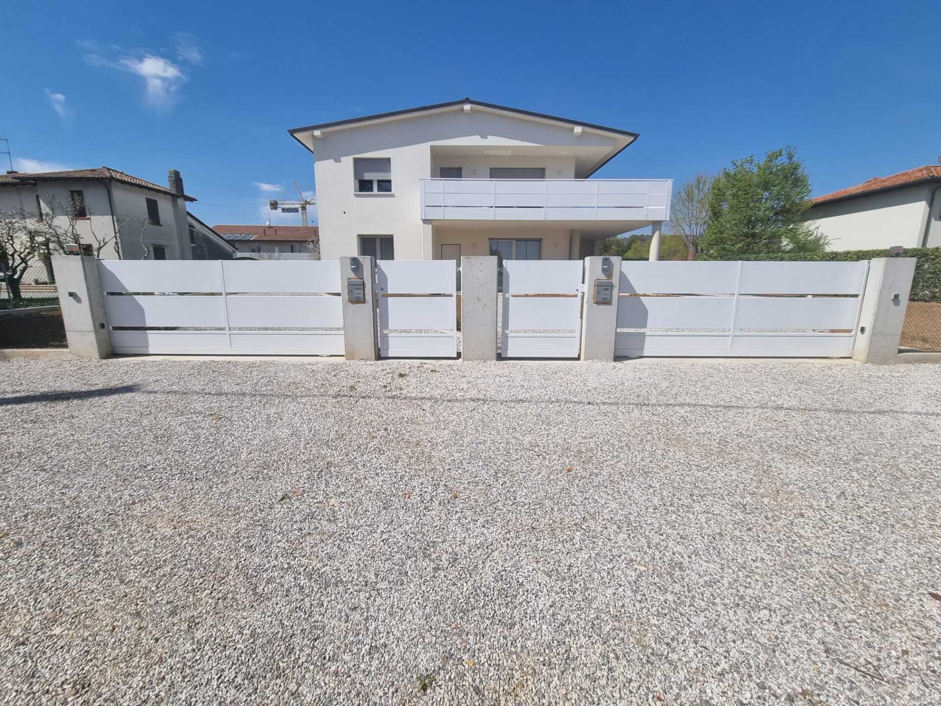 Casa bianca dietro una recinzione bianca con ghiaia grigia davanti in una giornata di sole.