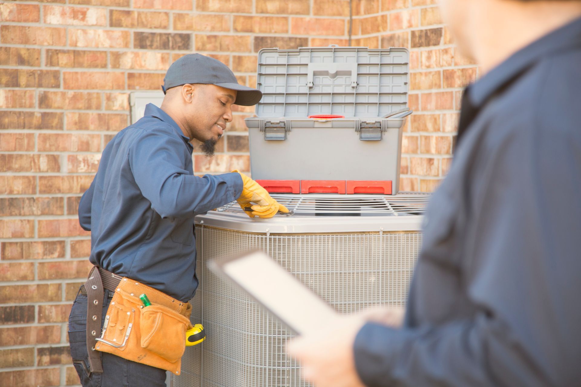 A man is working on an air conditioner while another man looks on.