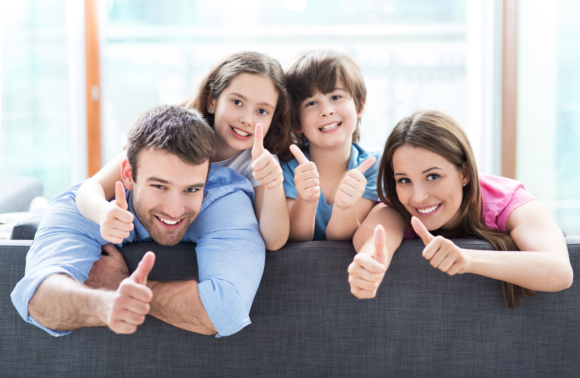 A family is giving a thumbs up while sitting on a couch.