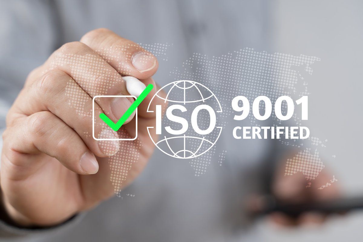 Main tenant un stylo et cochant en vert un texte certifié ISO 9001 et une icône de globe terrestre