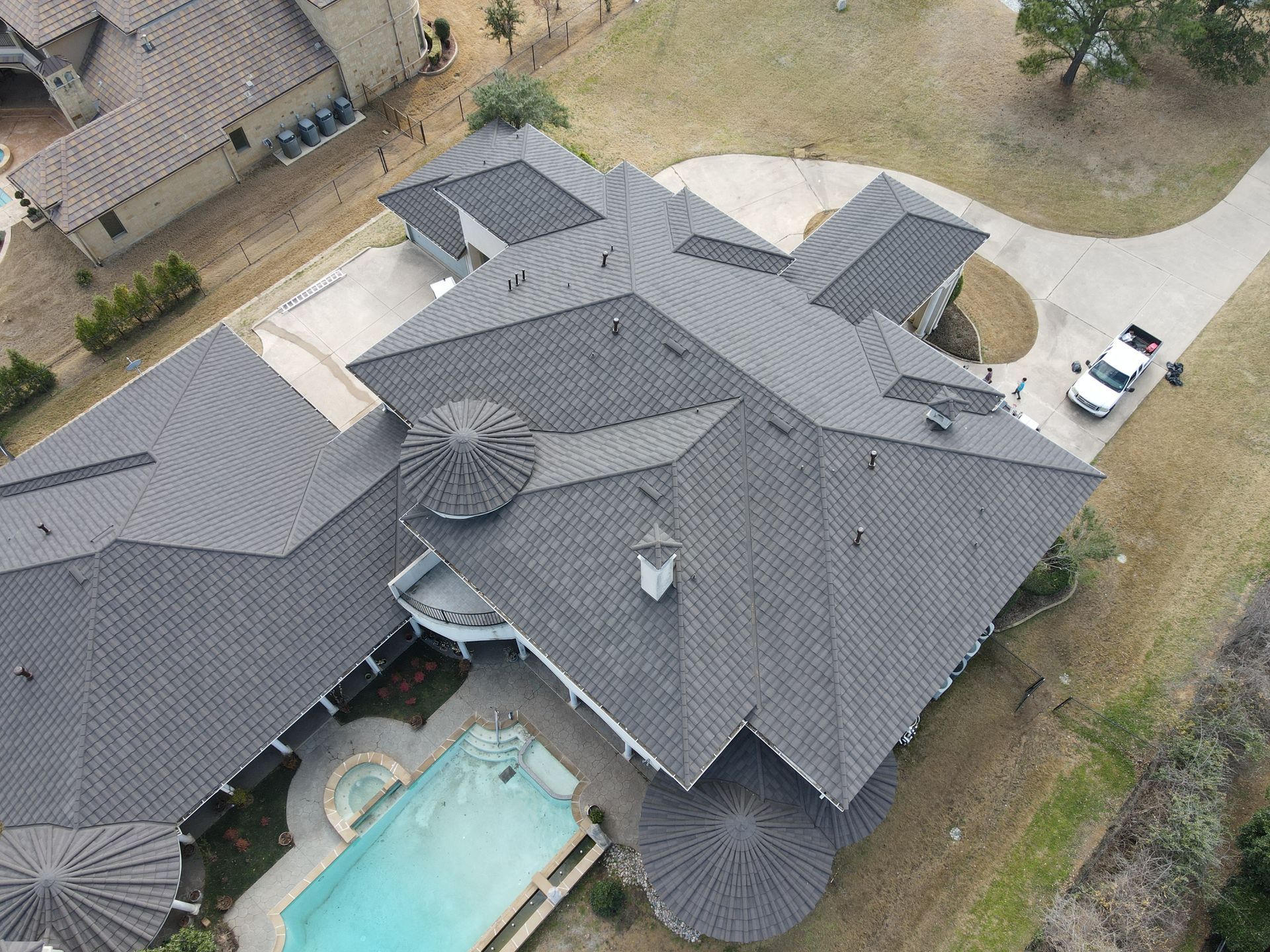 Aerial view of a large gray-roofed house with a backyard pool and driveway.