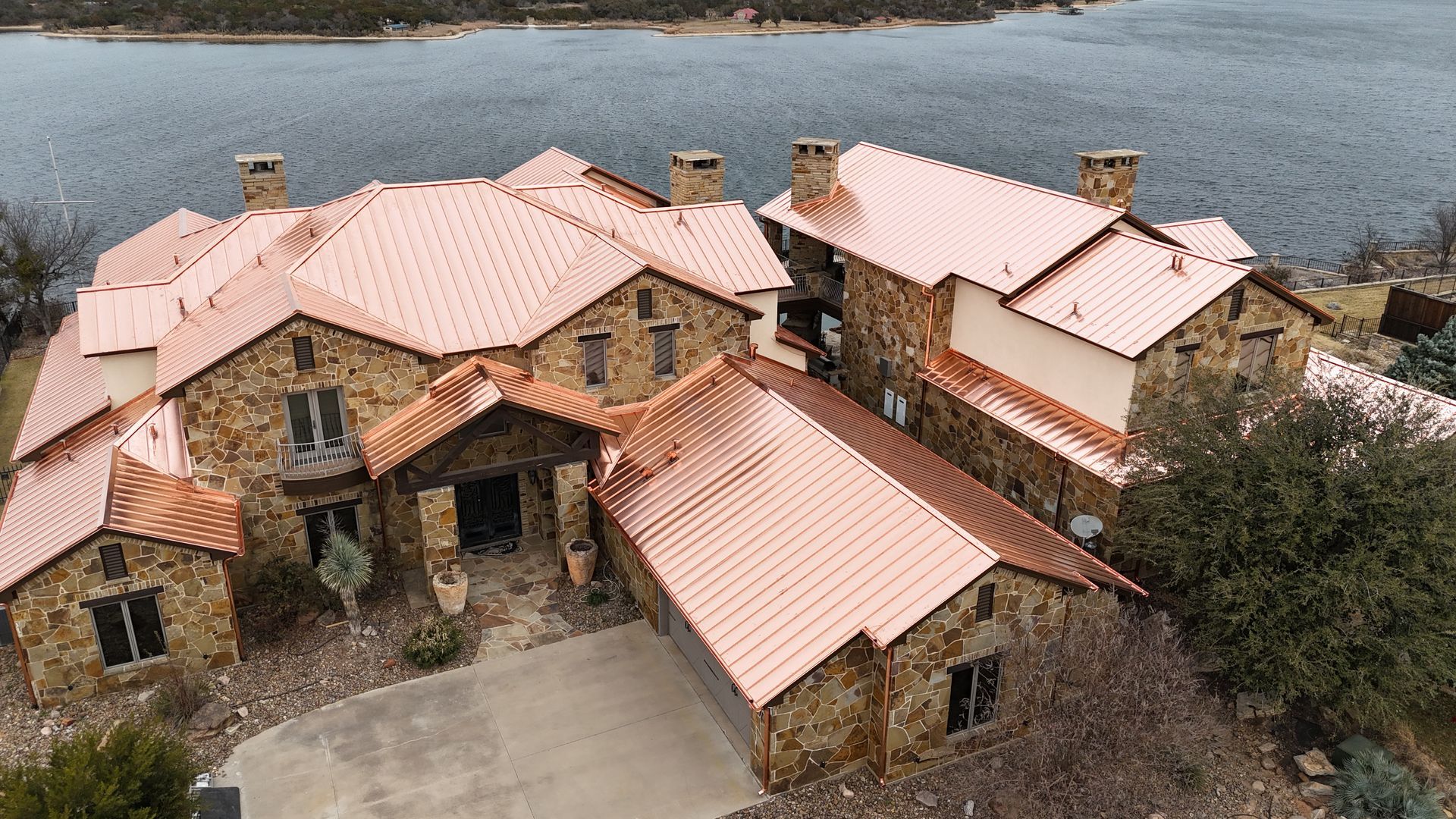 Stone house with red-tiled roofs beside a body of water, viewed from above