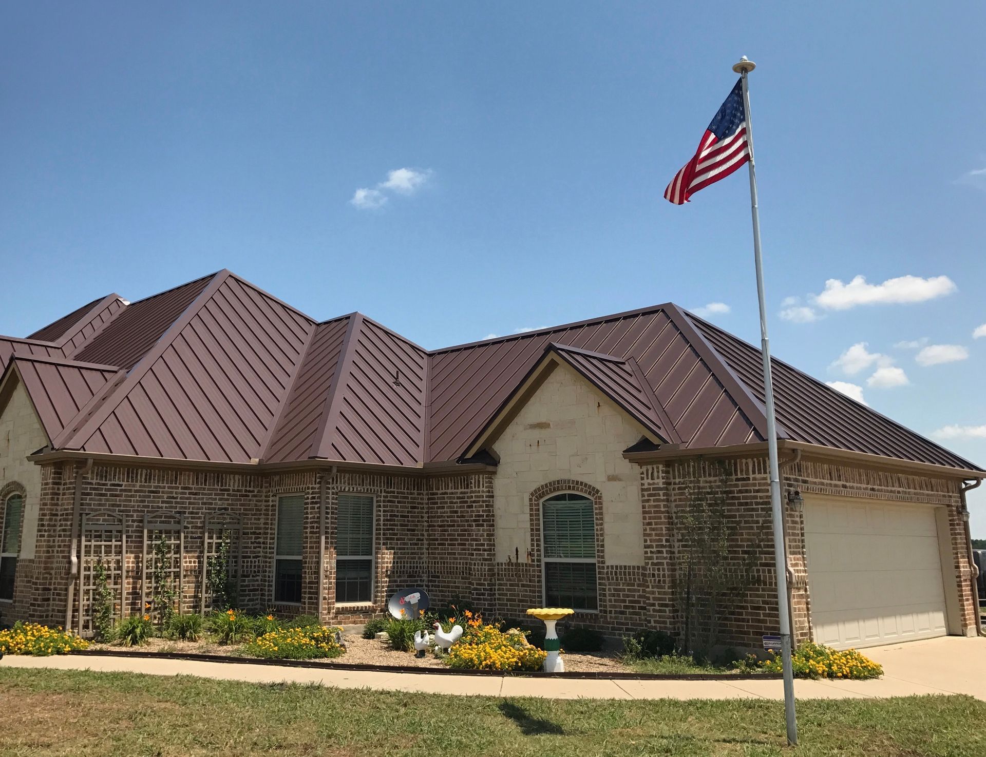 Single-story brick house with a brown roof and an American flag flying in front.