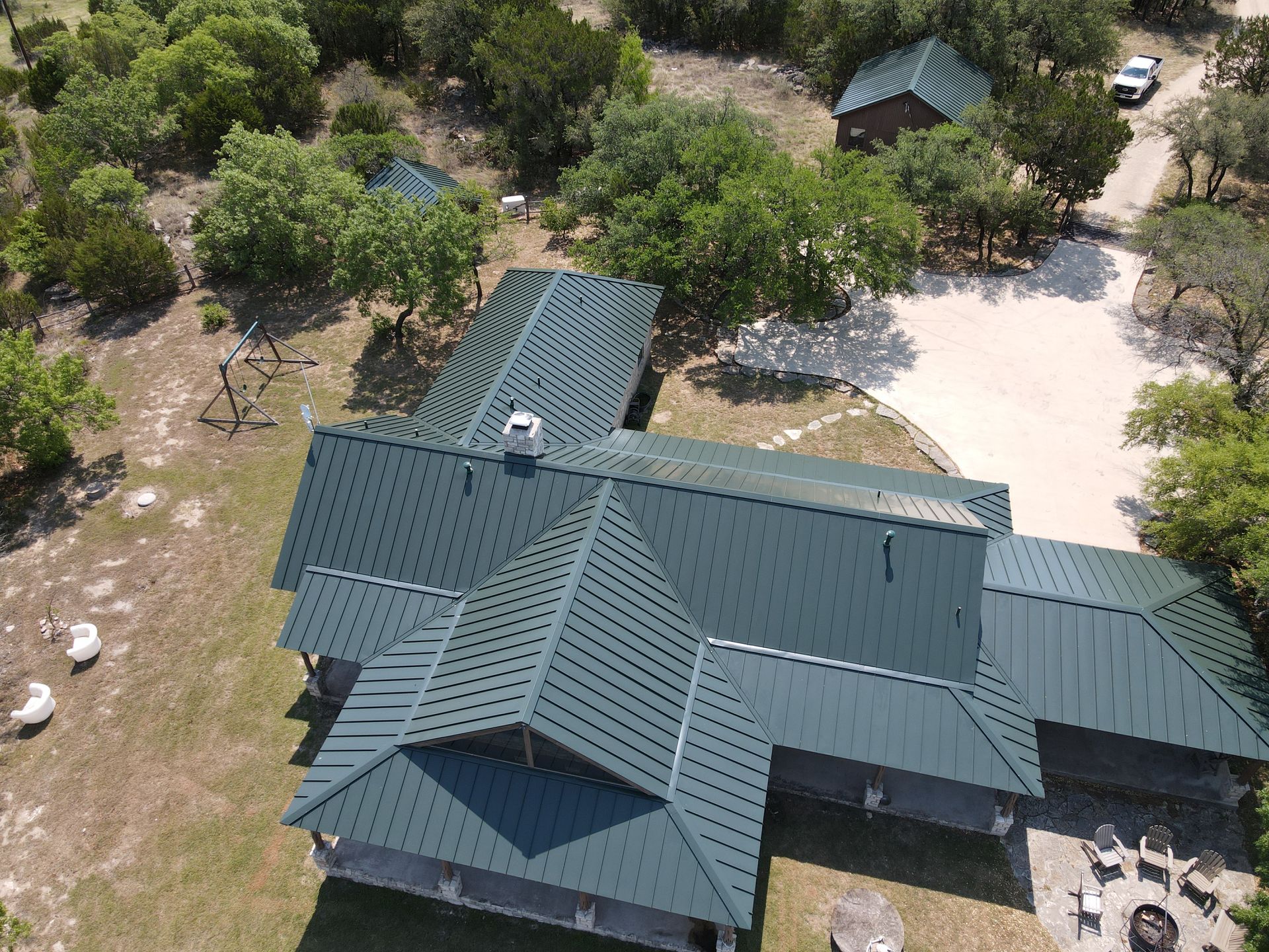 Aerial view of a brown shingled roof with a central ridge and surrounding greenery