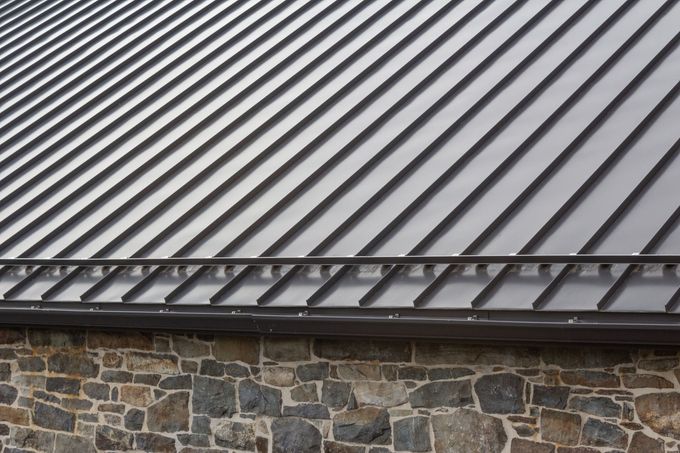 Metal roof with evenly spaced gray panels above a stone wall