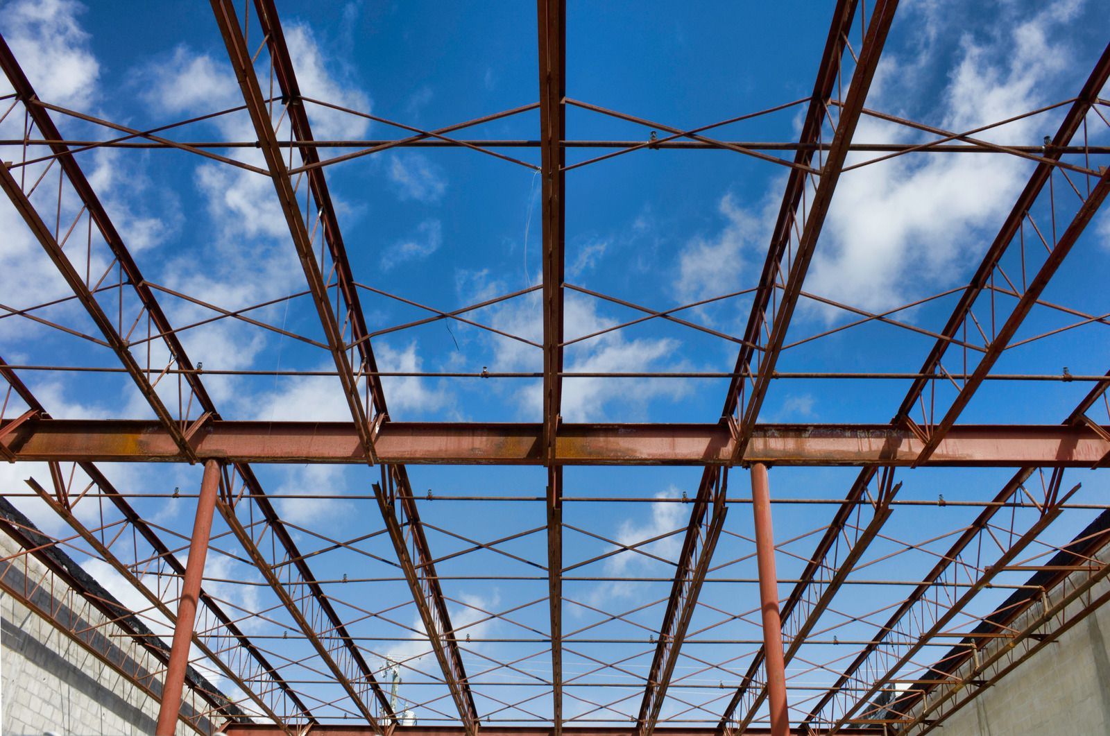 Rusty metal framework overhead against a blue sky with scattered clouds