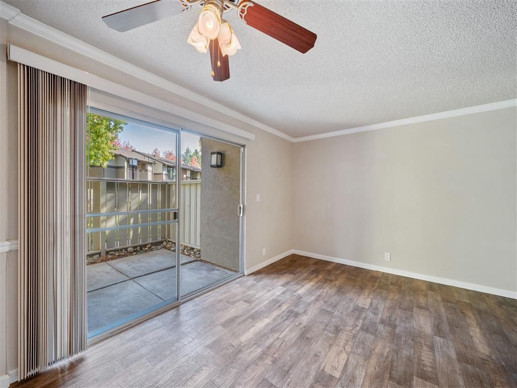 Empty living room with sliding glass door to a small patio, ceiling fan, and wood-look flooring at Valley Ridge Apartments.