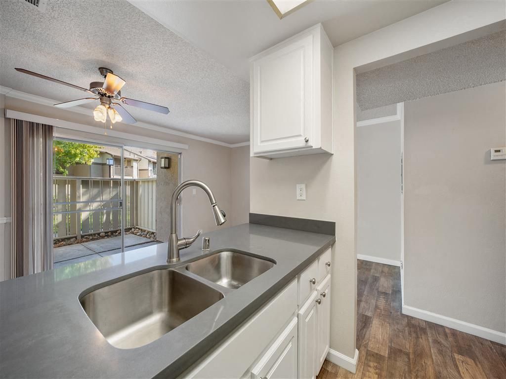 Kitchen with double sink, gray countertops, white cabinets, and a sliding glass door to the patio at Valley Ridge Apartments.