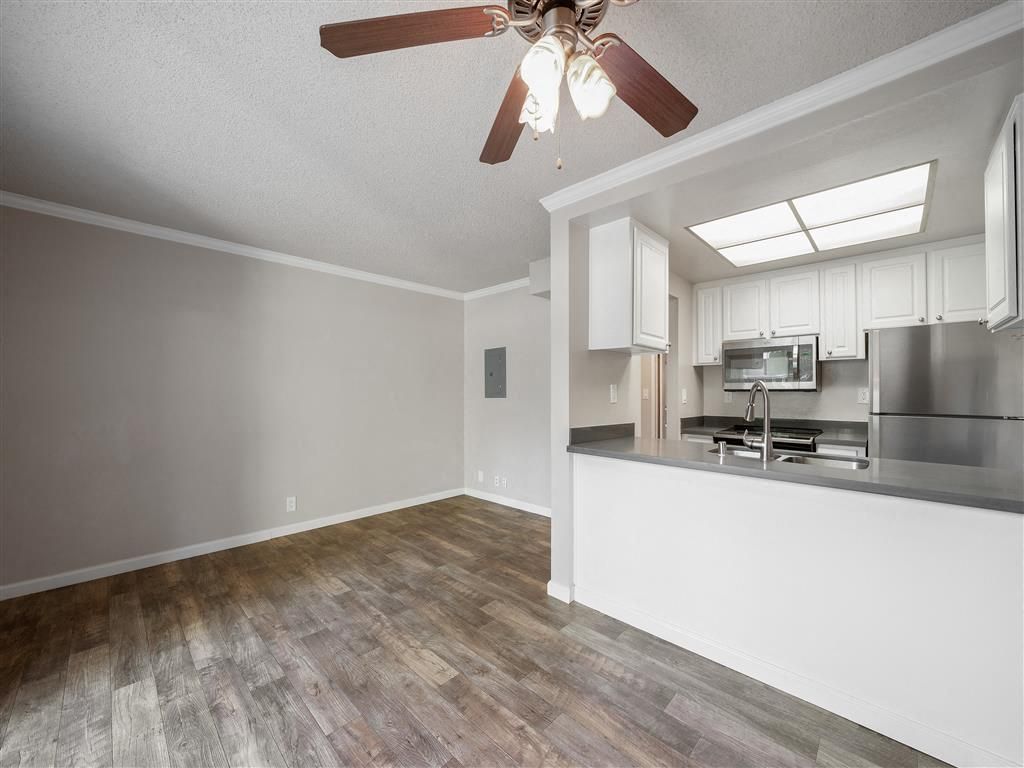 Open-concept kitchen and living area with white cabinets, stainless steel appliances, and a ceiling fan at Valley Ridge Apartments.