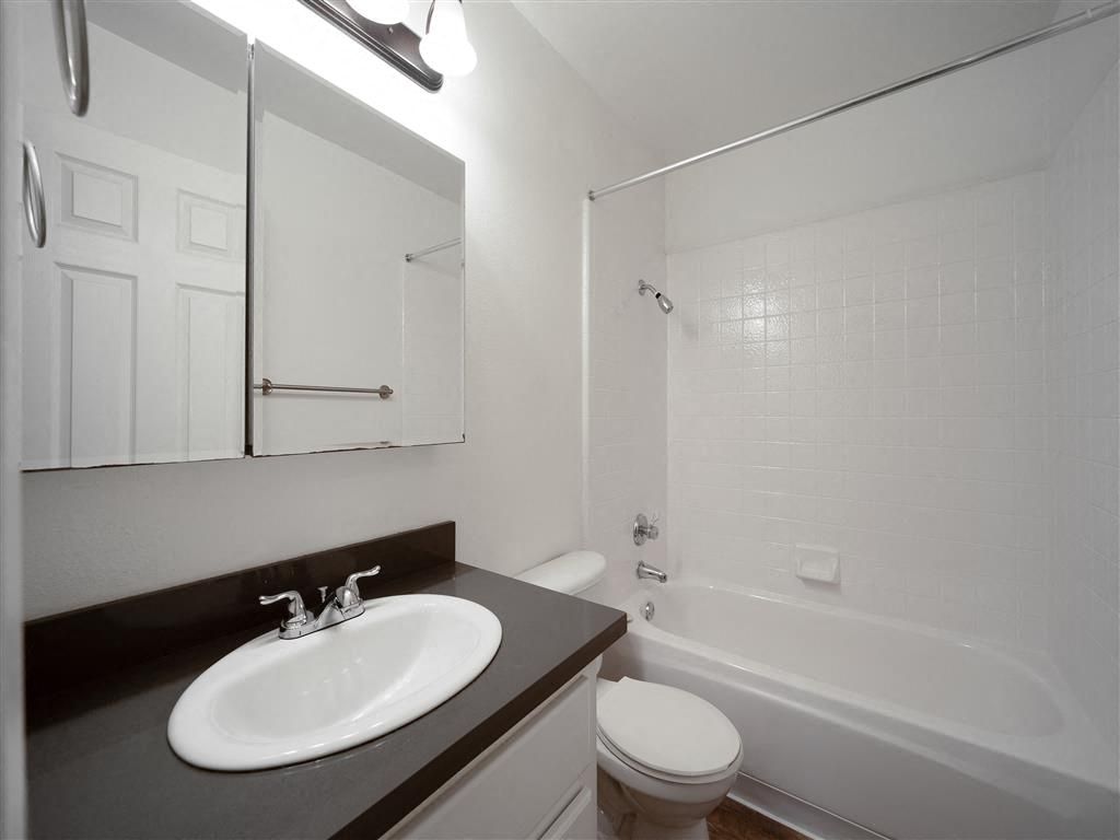 Bathroom with white tile tub/shower, sink, mirror, and toilet at Valley Ridge Apartments.
