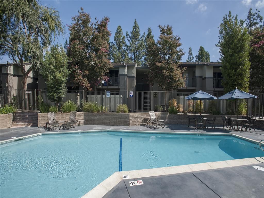 Outdoor apartment community pool with lounge chairs and umbrellas along the deck at Valley Ridge Apartments.