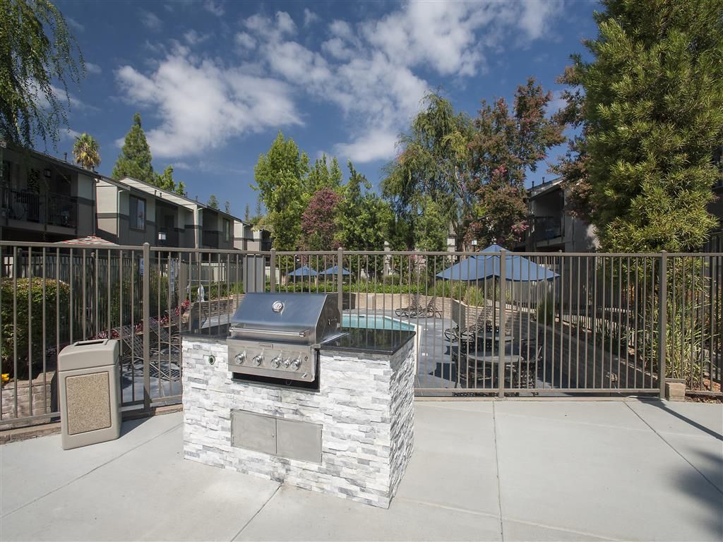 Outdoor communal BBQ grill area with a fenced pool and lounge seating at Valley Ridge Apartments.