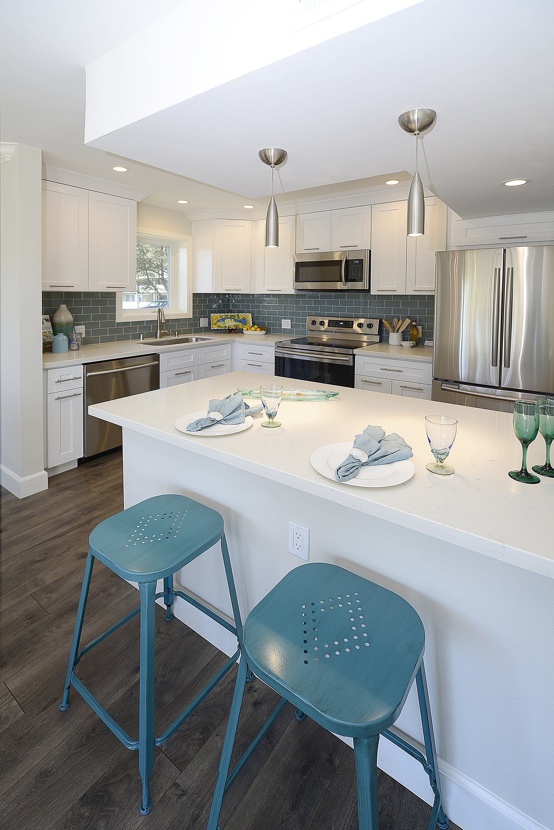 Bright modern kitchen with white island, blue stools, stainless appliances, and hanging pendant lights
