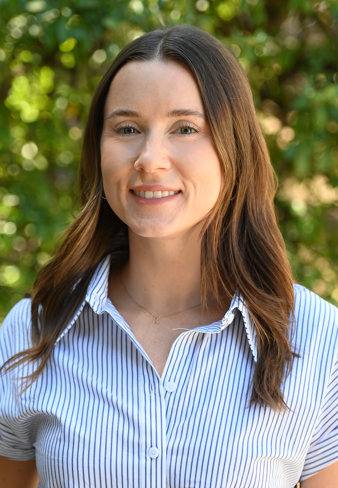 Portrait of a smiling woman in a white shirt against a green leafy background