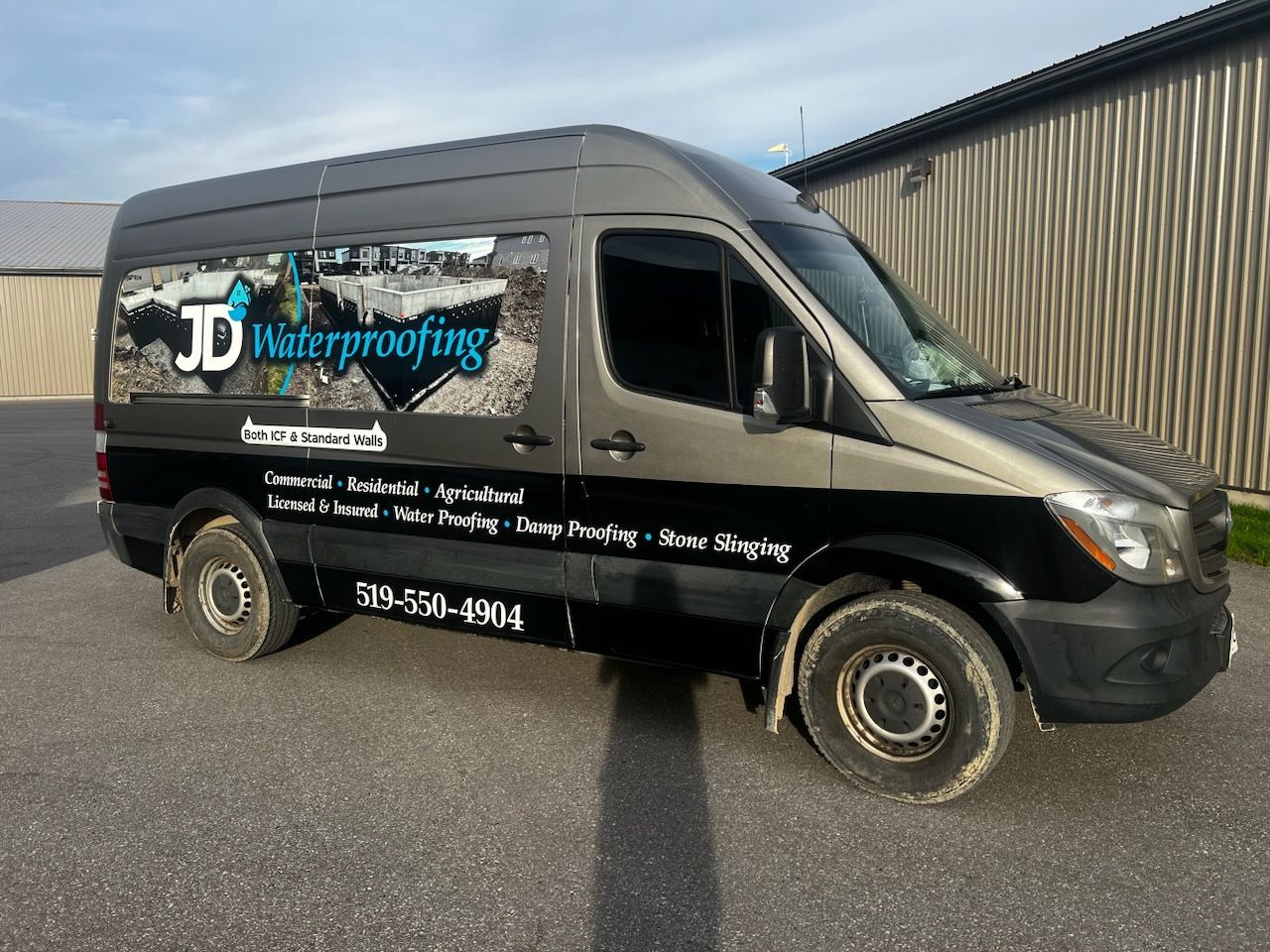 A JD Waterproofing van has the side advertising its services such as waterproofing, dampproofing, and stone slinging.