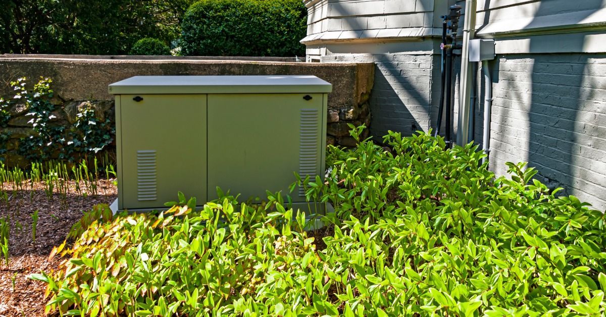 A residential standby generator on a pad outside a grey brick home.